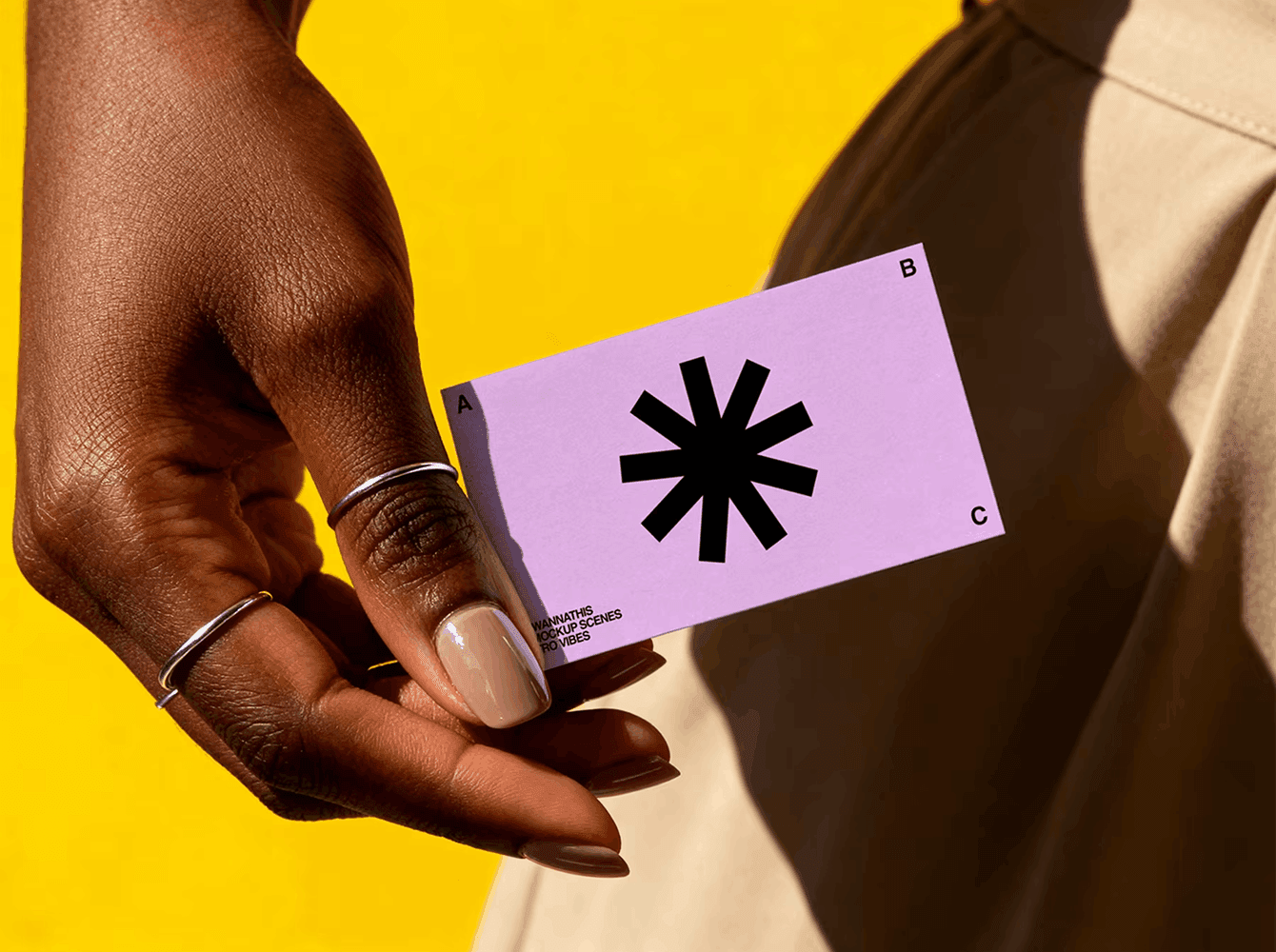 Lilac business card mockup with bold black asterisk logo, held in hand against a bright yellow backdrop — a presentation scene for showing brand identity in print.
