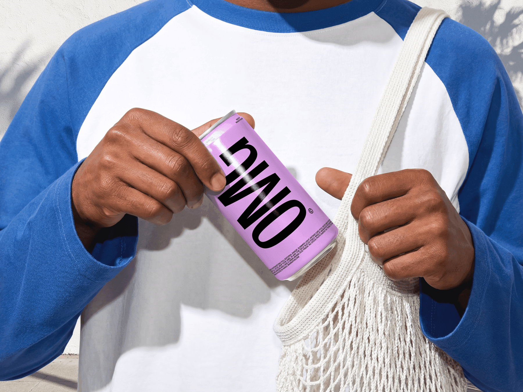 Person holding a beverage can mockup next to a tote bag