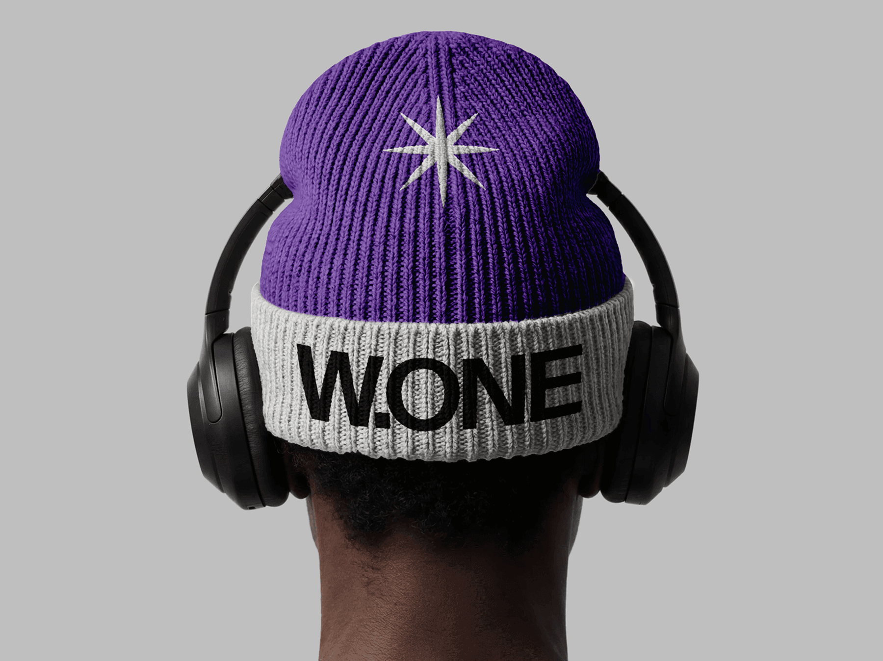 Back view of a person wearing a beanie with over-ear headphones in a studio setting