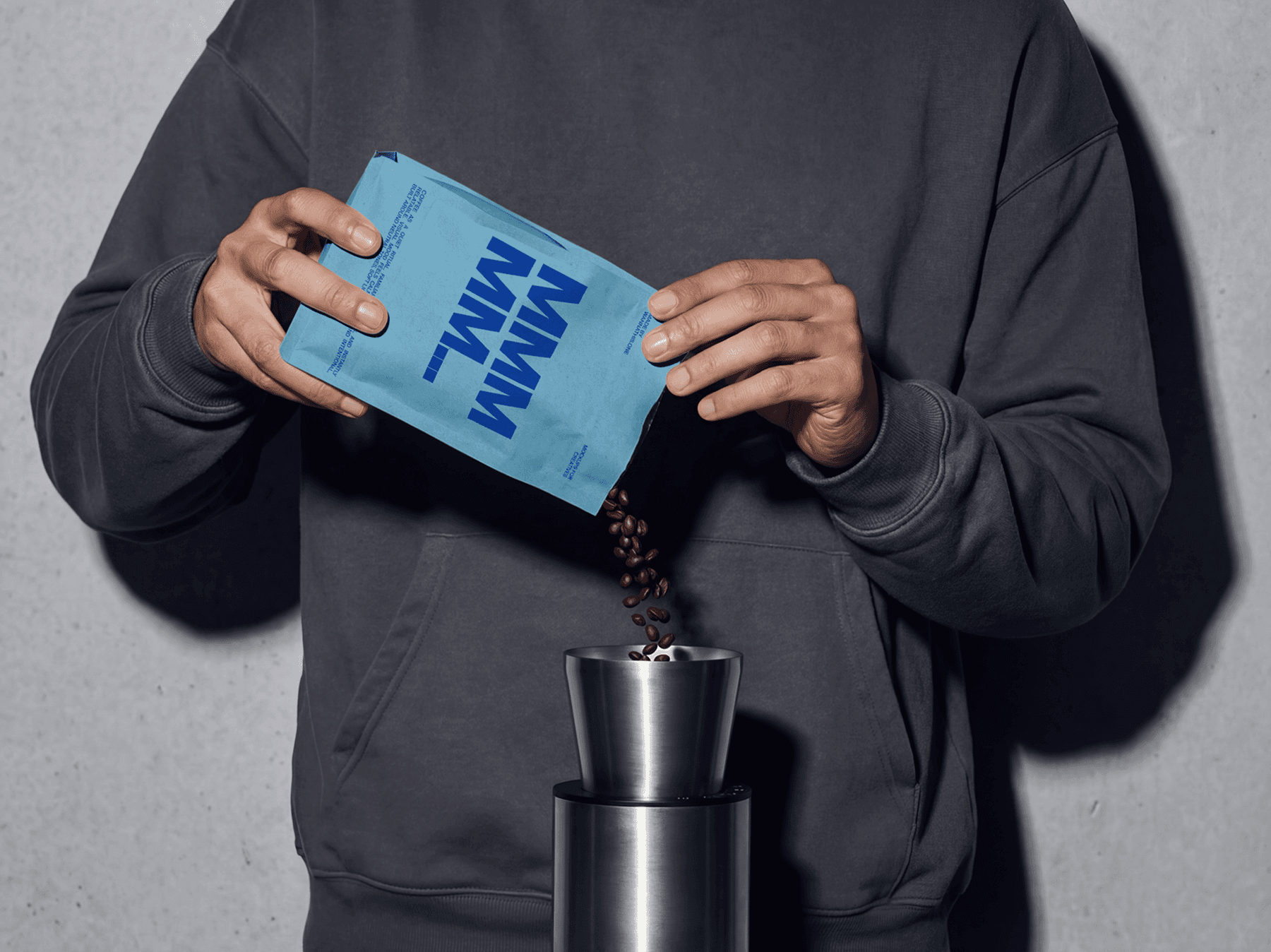Person pouring coffee beans from a pouch into a grinder indoors