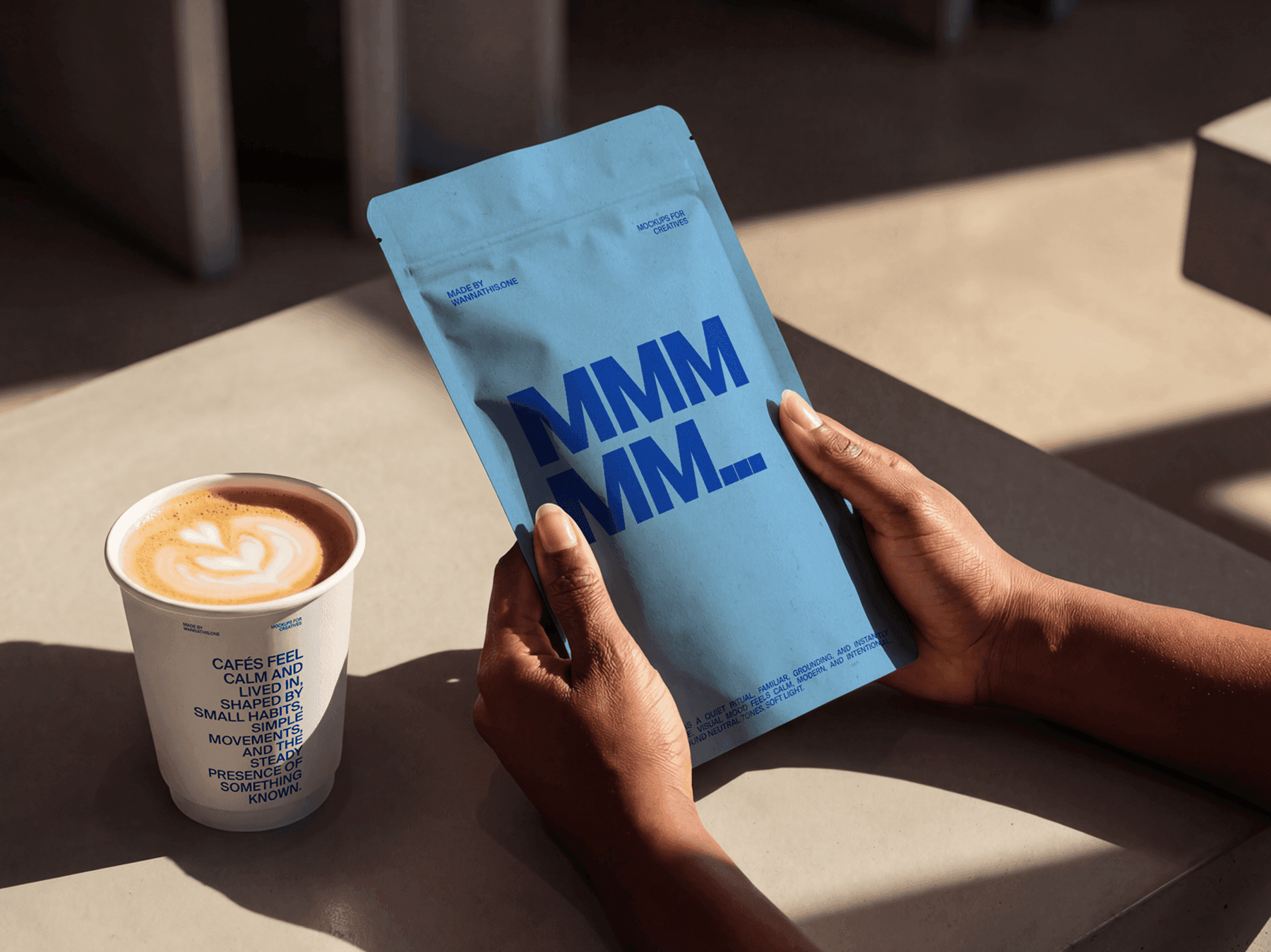 Person holding a coffee bag next to a takeaway cup on a table