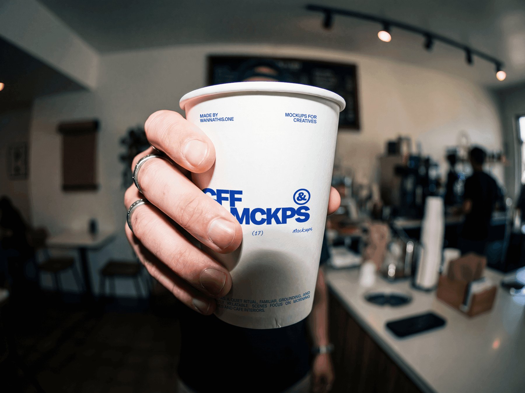 Person holding a takeaway coffee cup inside a cafe setting
