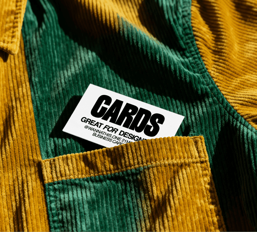 Free business card mockup resting on a yellow and green corduroy shirt with ribbed fabric texture in warm natural light.