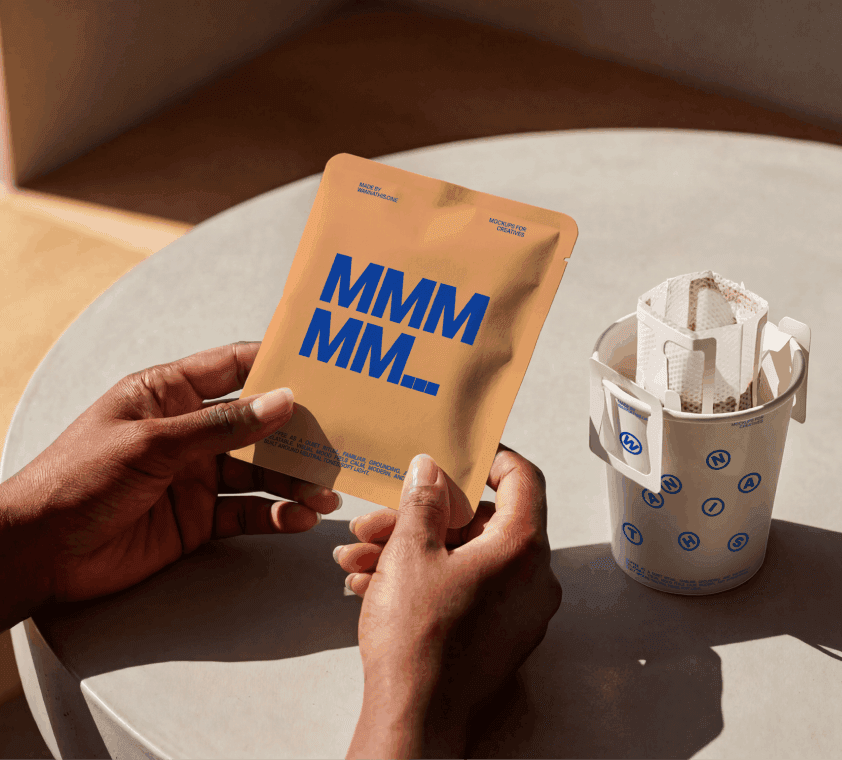 Drip coffee bag packaging mockup held in hands next to cup in warm natural light