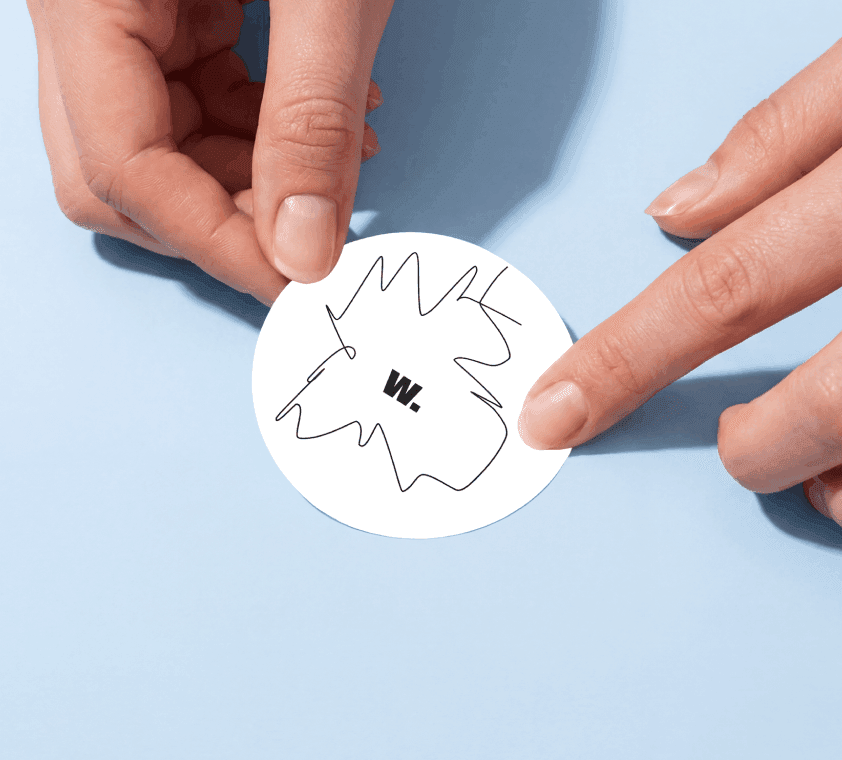 Round sticker mockup pinched between fingers with a second hand pointing at its edge.