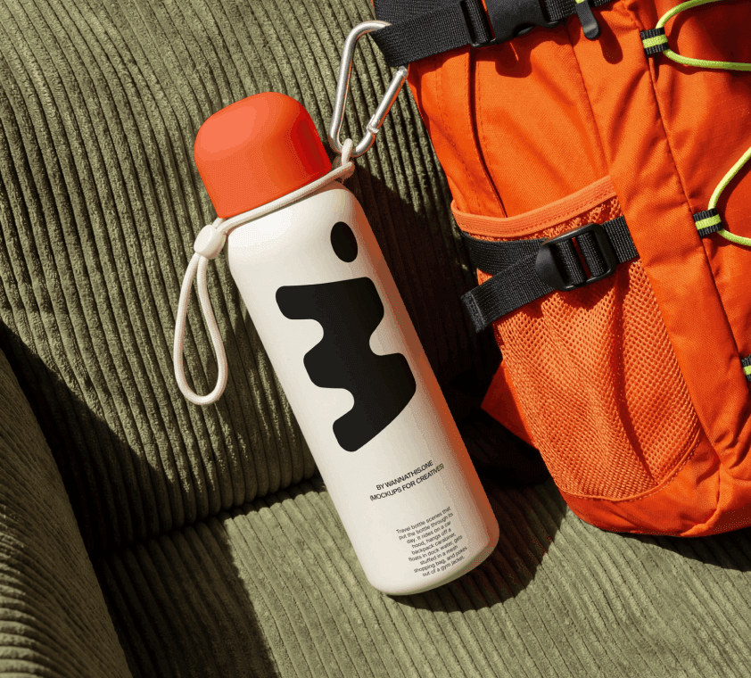 Travel water bottle mockup with a red cap and abstract black mark, clipped by a carabiner to an orange backpack, resting on green corduroy.