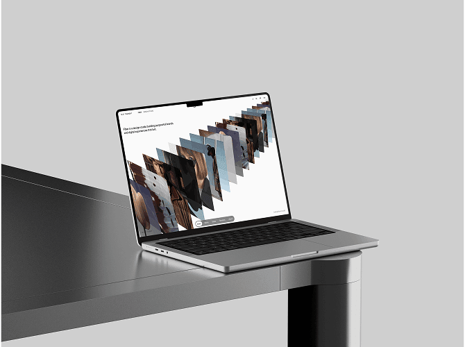 Fiber Framer portfolio template on a MacBook at a grey desk edge, a fanned stack of project images across a white layout, a minimal template for design studios