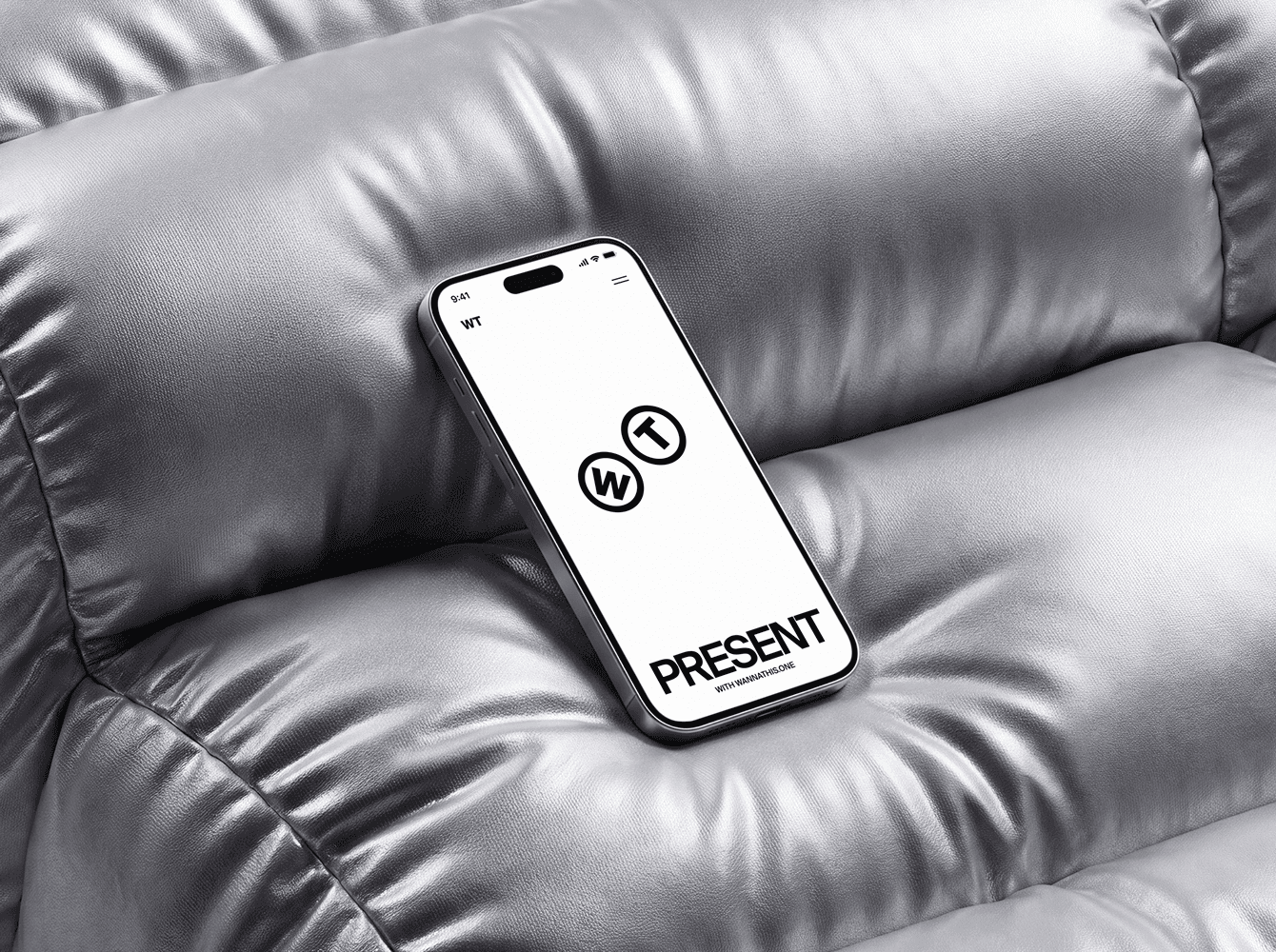 An iPhone mockup resting on a silver leather sofa showing a clean black and white PRESENT app screen, an example of a realistic phone mockup for presenting design