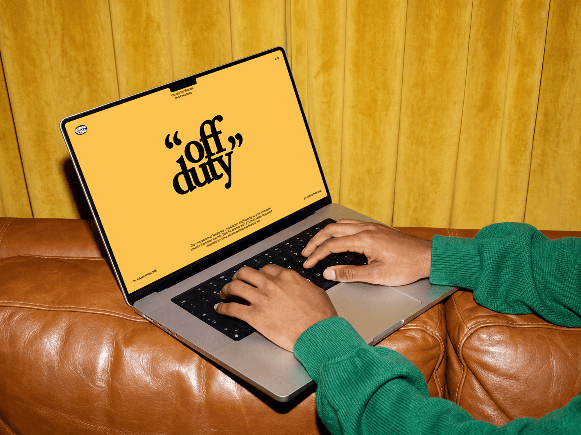 MacBook open on a leather sofa with both hands resting on the keyboard