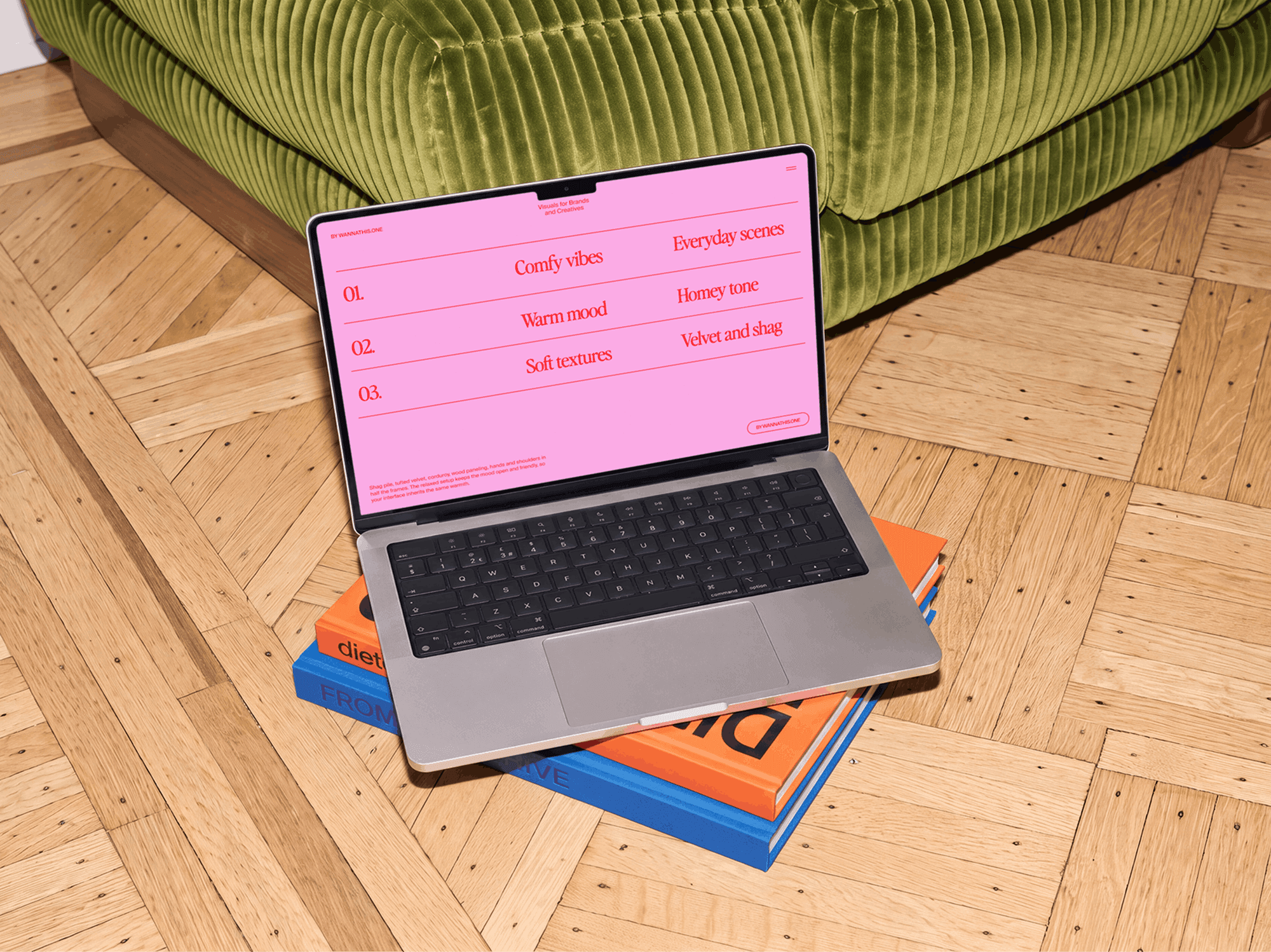 Open MacBook resting on a stack of books beside a sofa in a living room