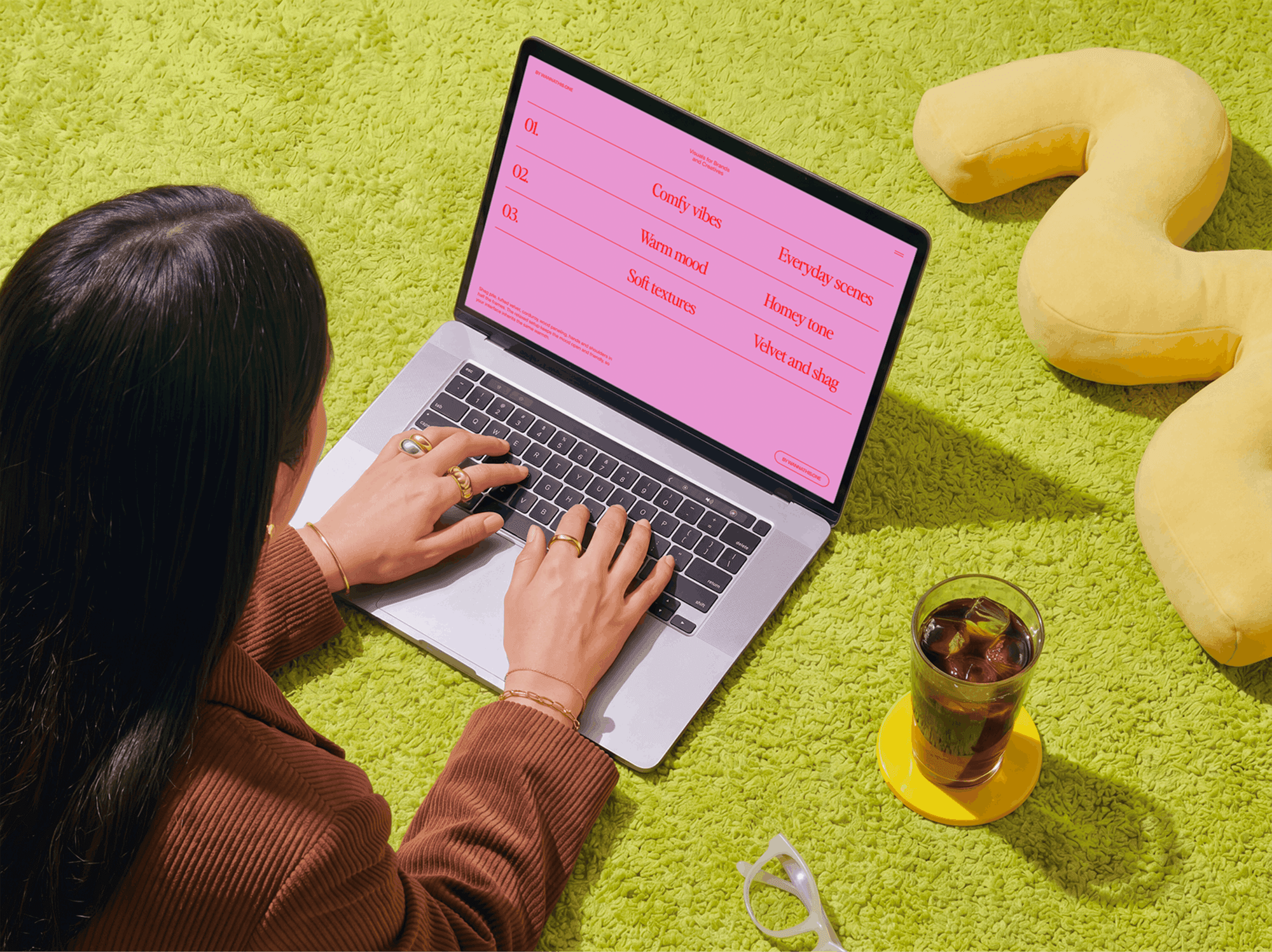 Person sitting on a soft carpet using a MacBook with accessories laid out nearby