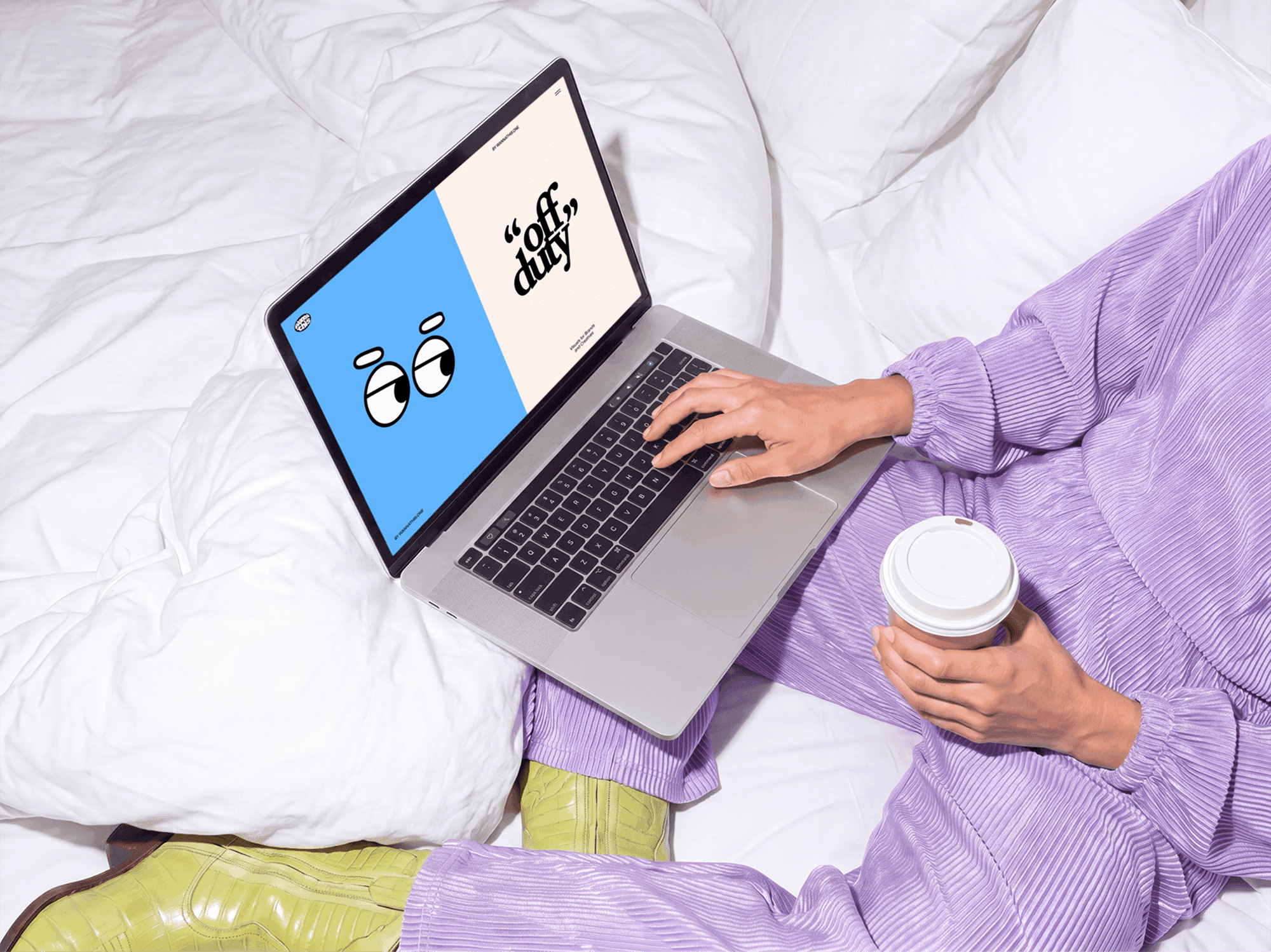 MacBook open on a bed with a person nearby holding a cup of coffee