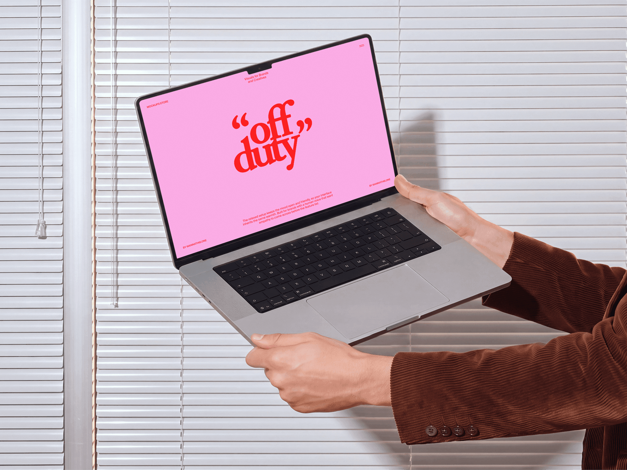 Open MacBook held in two hands in front of a window covered by blinds