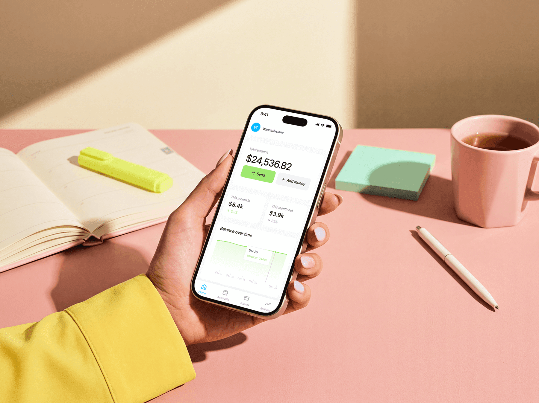 Hand holding an iPhone mockup above a studio desk with notebooks and tools