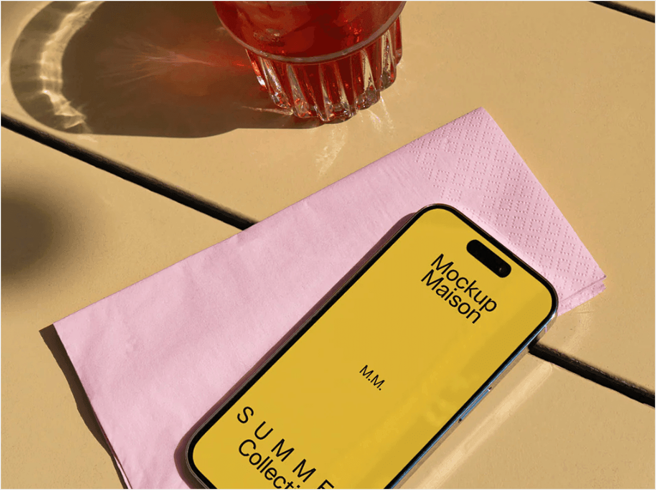 iPhone mockup with yellow screen on pink napkin next to glass of red drink on outdoor table