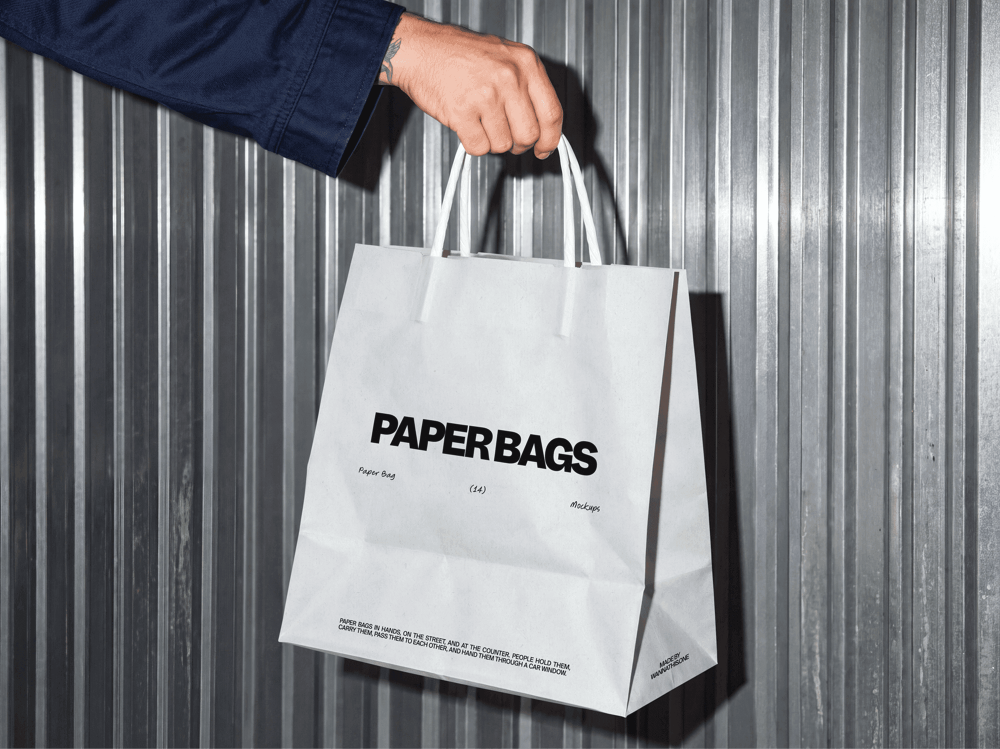 Paper shopping bag mockup hanging from one hand in front of a ribbed metal wall