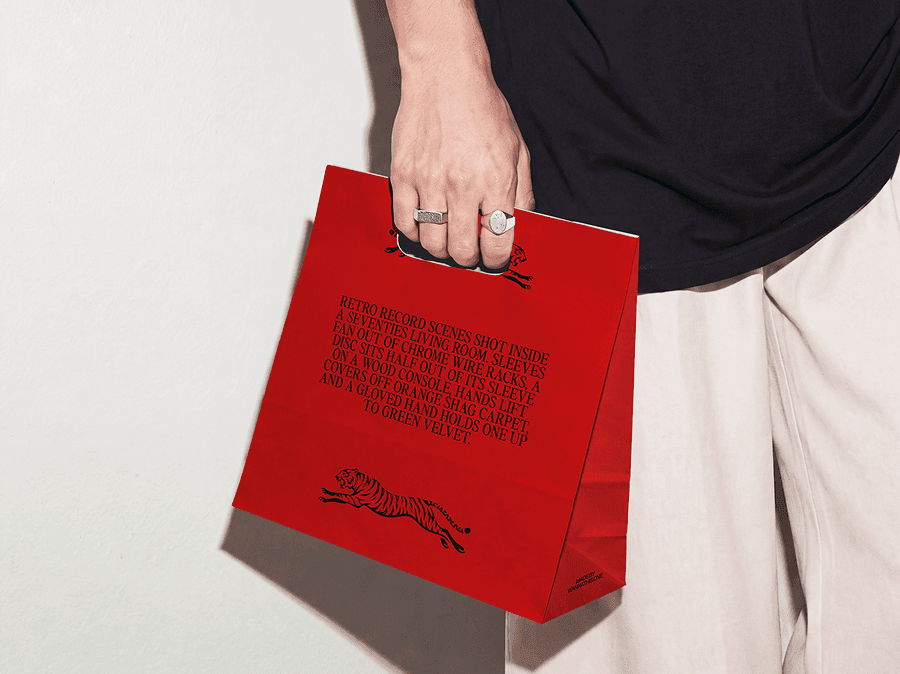 Paper shopping bag mockup carried at waist height by a person against a white wall
