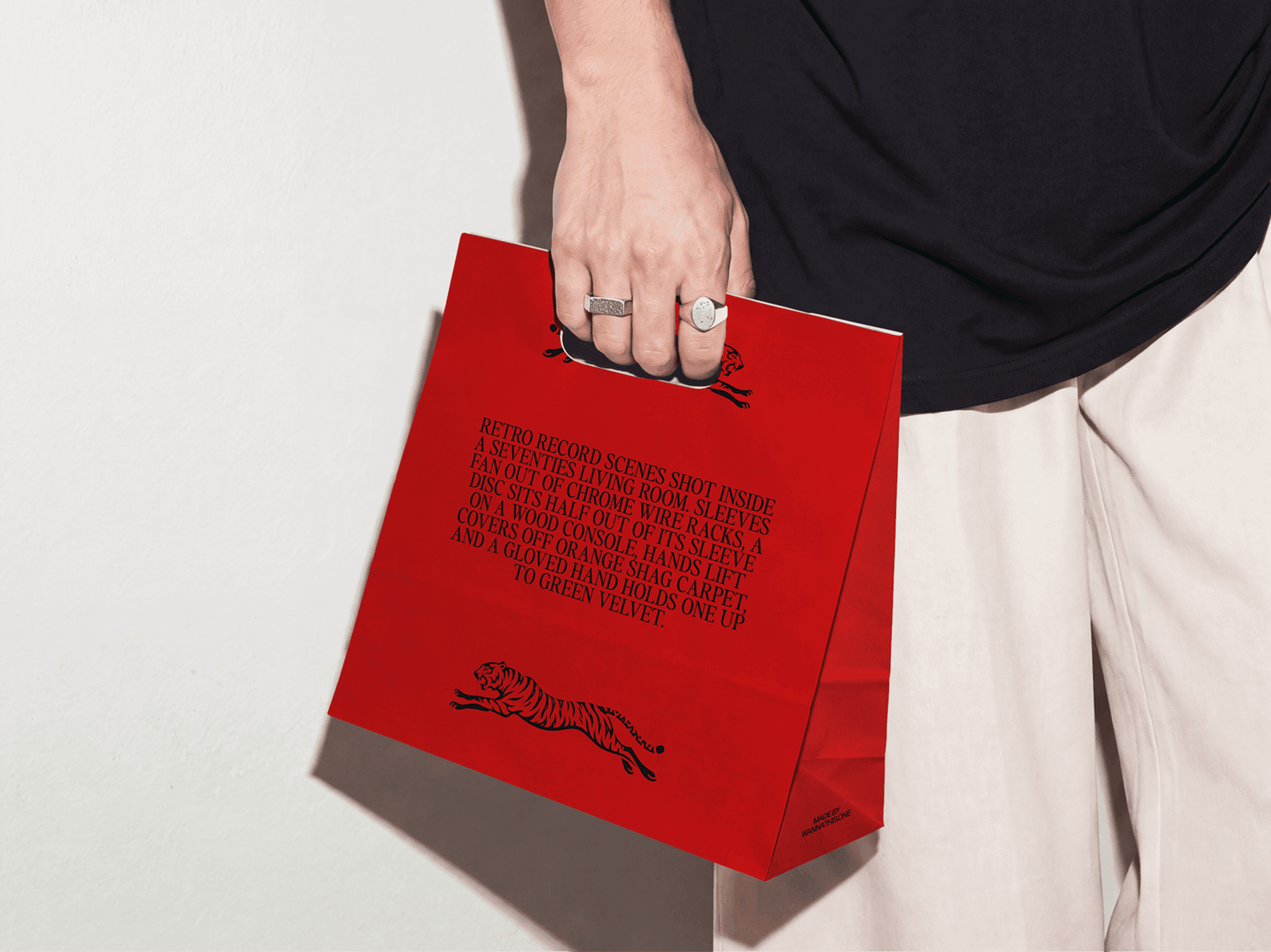 Paper shopping bag mockup carried at waist height by a person against a white wall