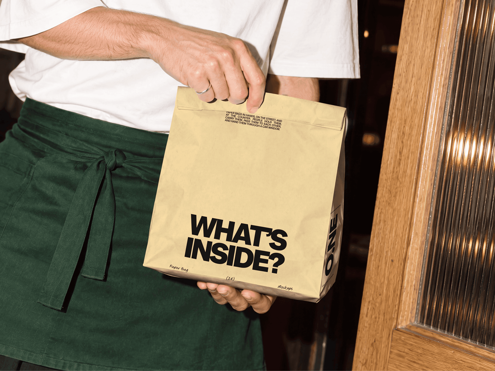 Folded takeaway paper bag mockup held by an aproned worker beside a wooden door