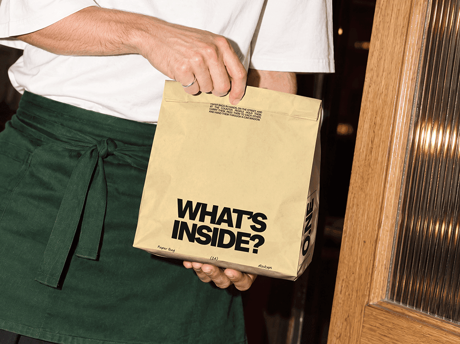 Folded takeaway paper bag mockup held by an aproned worker beside a wooden door