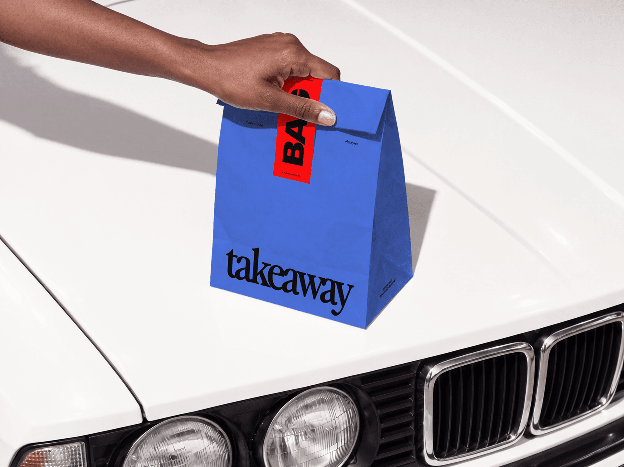 Folded takeaway paper bag mockup steadied by one hand on the hood of an old car