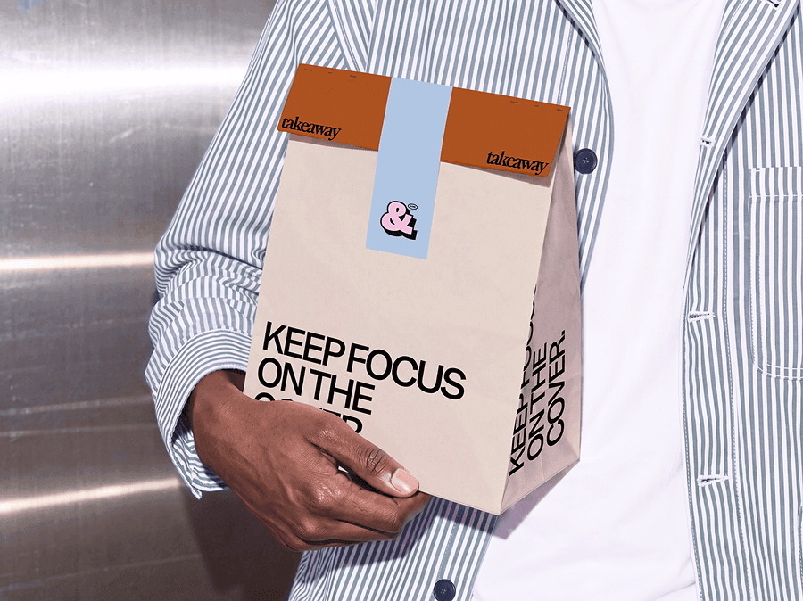 Folded takeaway paper bag mockup cupped in two hands in front of a vending machine