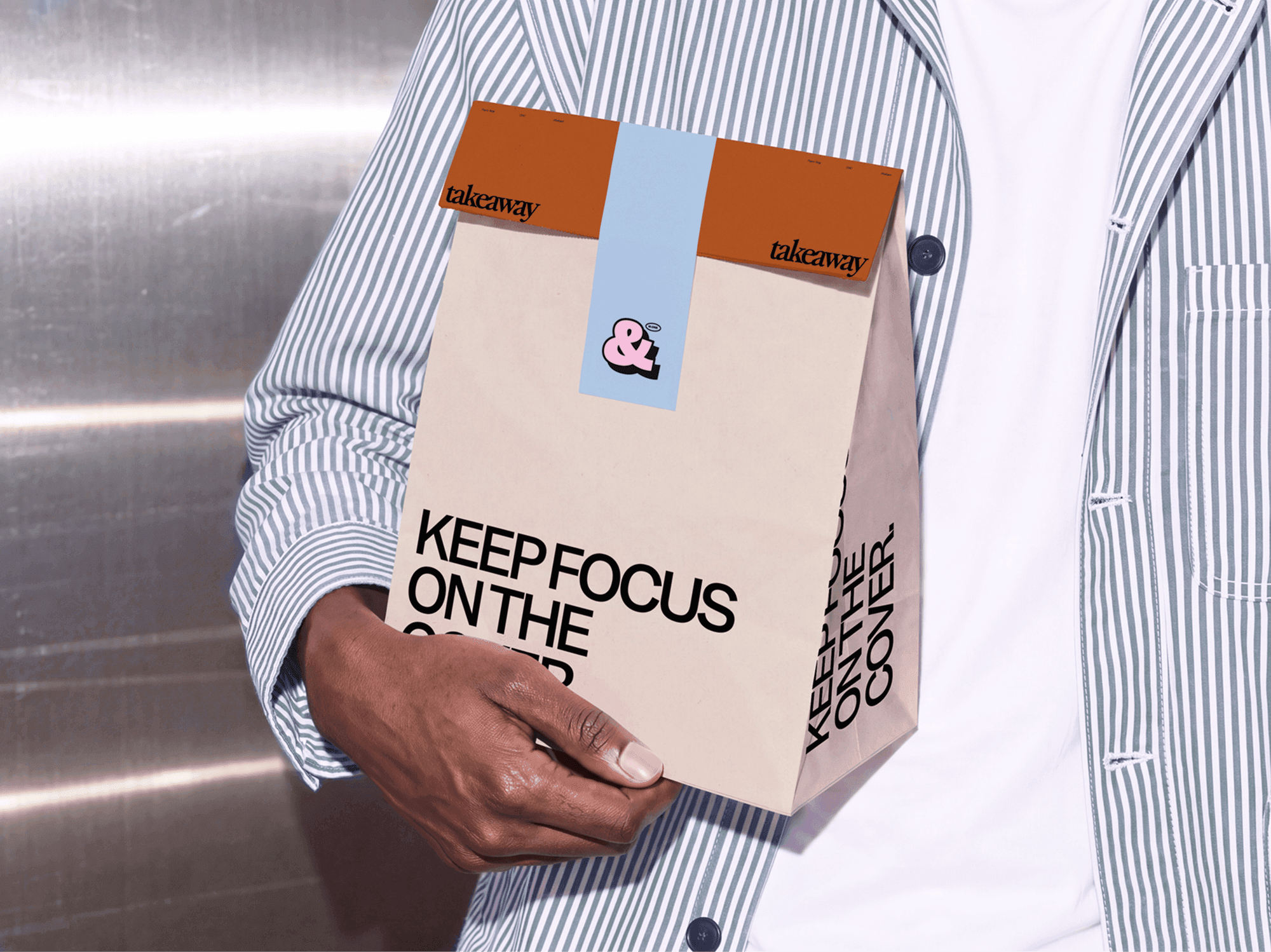 Folded takeaway paper bag mockup cupped in two hands in front of a vending machine