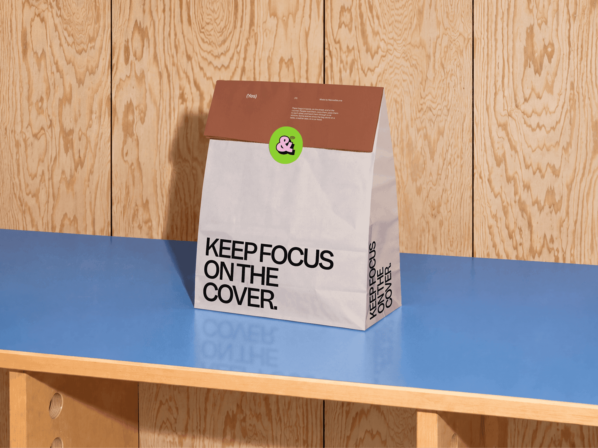 Folded takeaway paper bag mockup standing alone on a blue table by a wooden wall