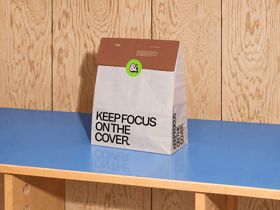 Folded takeaway paper bag mockup standing alone on a blue table by a wooden wall