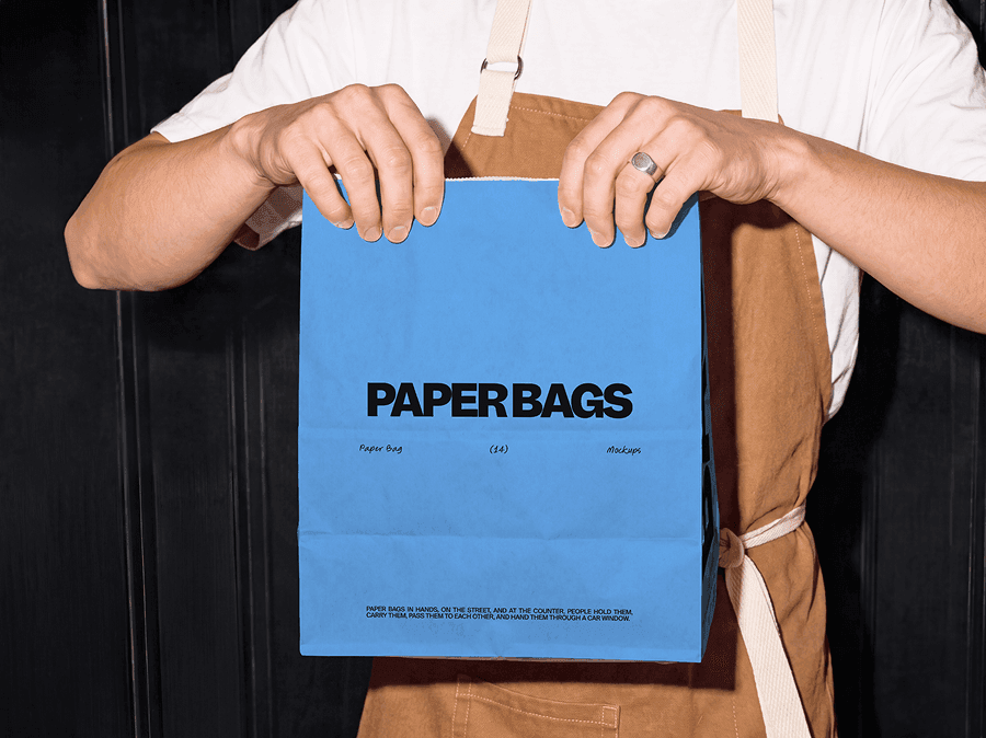 Takeaway paper bag mockup held out by a cafe worker wearing a dark canvas apron