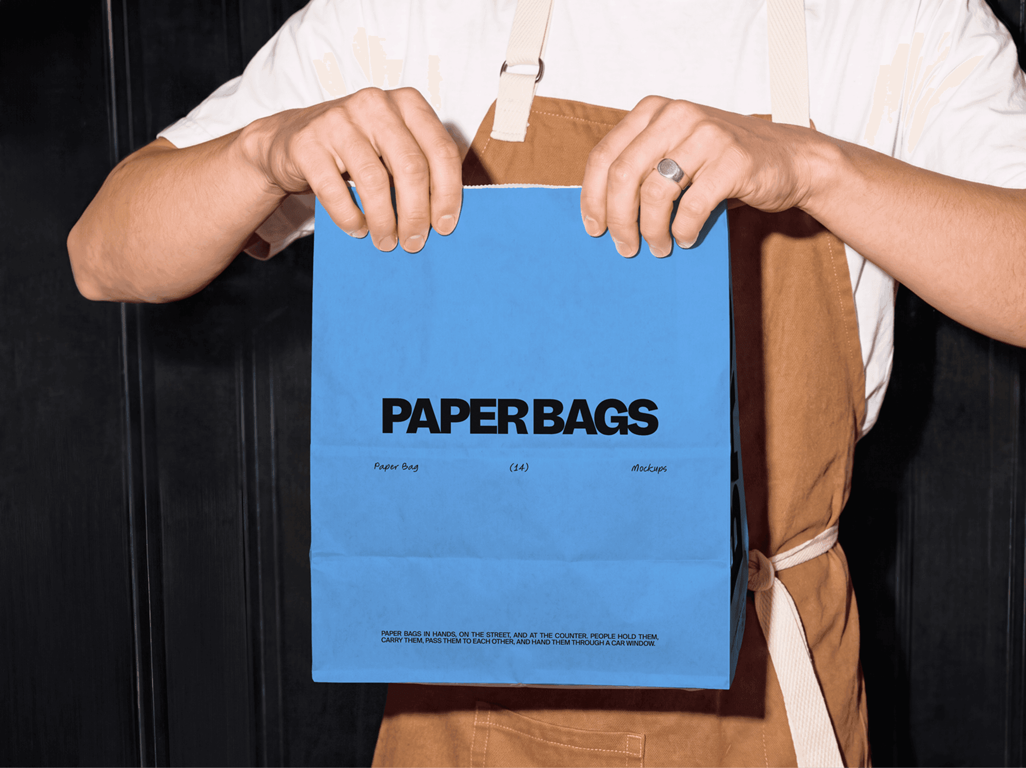 Takeaway paper bag mockup held out by a cafe worker wearing a dark canvas apron