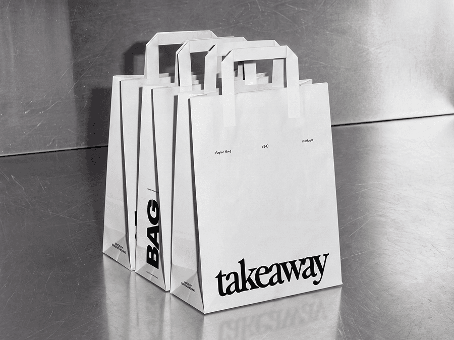 Several paper shopping bag mockups with handles lined up along a metal counter