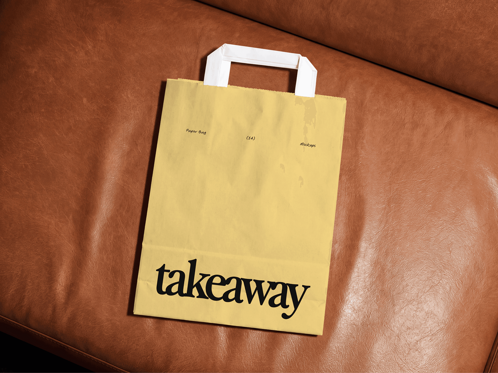 Paper shopping bag mockup with handles sitting upright on a brown leather sofa