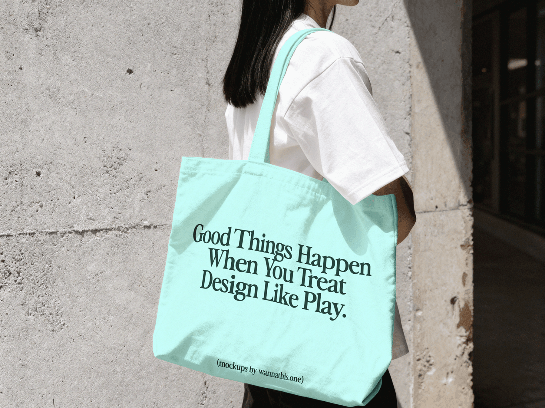 Tote bag mockup worn by a person walking near a concrete wall